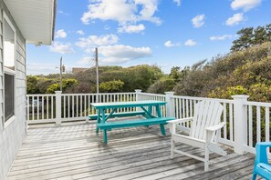 A wooden deck with a picnic table and chairs, surrounded by white railings and greenery. - Pool| Close to Beach| Sleeps 10 (Emerald Isle)