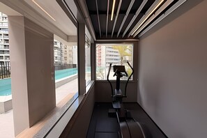 Ein modernes Zimmer mit Fenster, Laufband und Blick auf Pool und Gebäude.