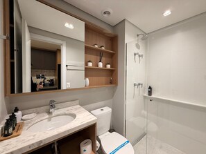 A modern bathroom with a marble sink, a toilet, a glass shower enclosure, and wooden shelves above the sink. - Condomínio Helbor Edition  (São Paulo)