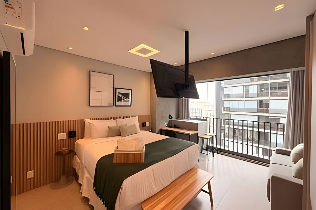 A modern hotel room with a large bed, a desk, a chair, and a balcony with a view of the city.