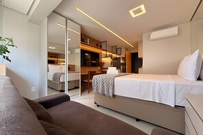 A modern hotel room with a bed, a sofa, a desk, and a kitchenette. - Condomínio Helbor Edition  (São Paulo)