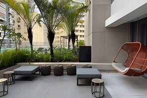 Eine Dachterrasse mit Außenmöbeln, darunter Stühle und Tische, umgeben von Grünflächen und Gebäuden.
