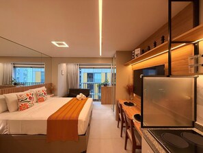 A modern hotel room with a bed, a desk, a refrigerator, and a view of the city. - Condomínio Helbor Edition  (São Paulo)