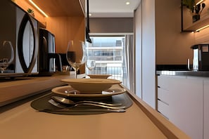 A modern kitchen with a large window, a dining table set with plates, cutlery, and glasses, and a view of a building outside. - Condomínio Helbor Edition  (São Paulo)