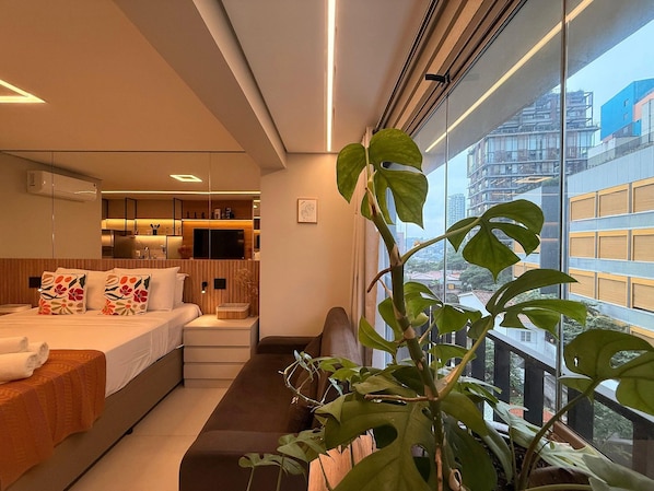 Quarto de hotel moderno com cama, mesa de cabeceira e uma grande janela com vista para a cidade.