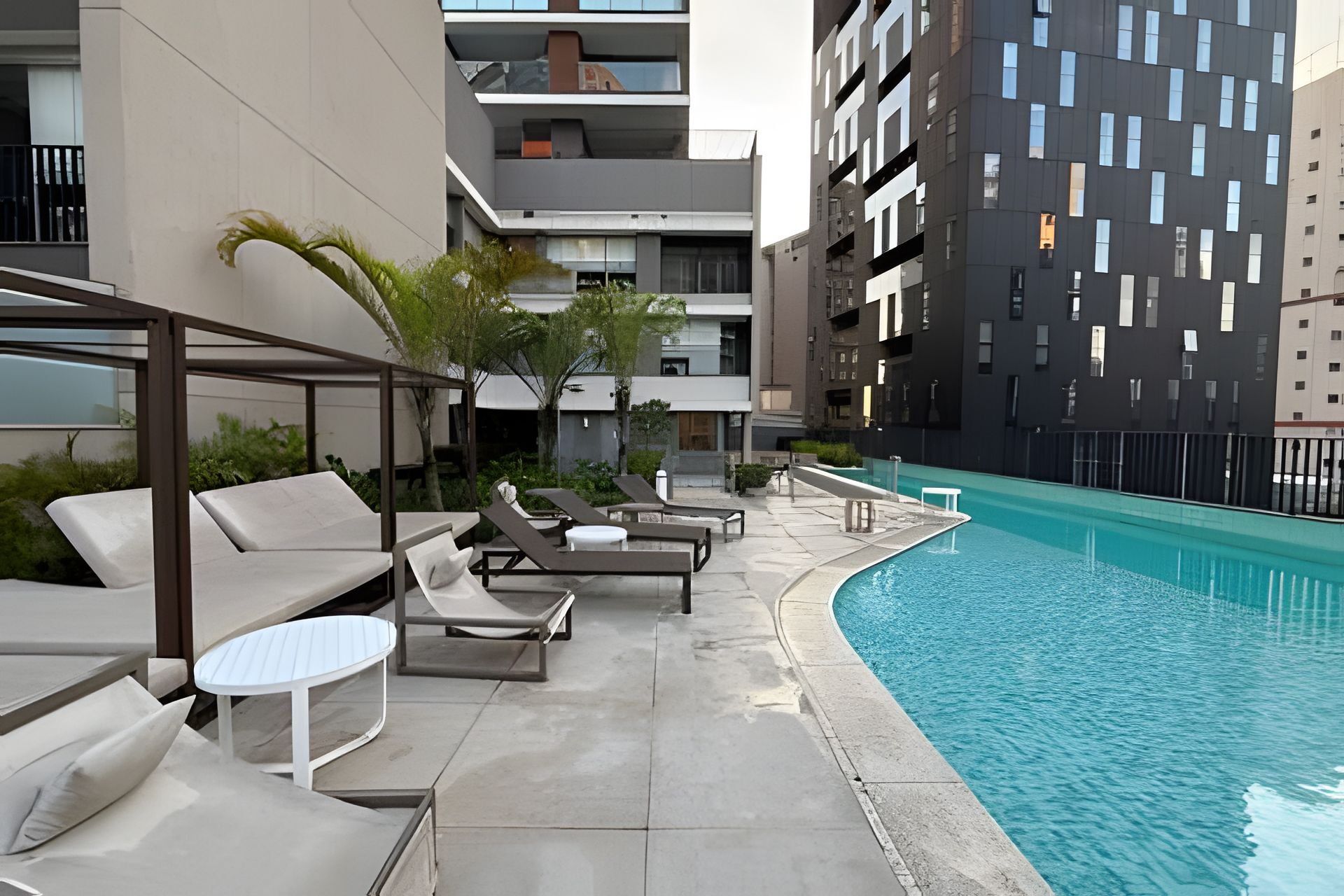 A rooftop pool area with lounge chairs and a small table, surrounded by modern buildings.