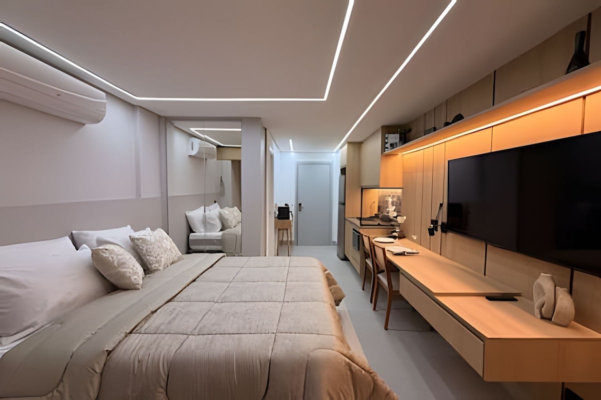A modern bedroom with a large bed, a desk, and a TV.