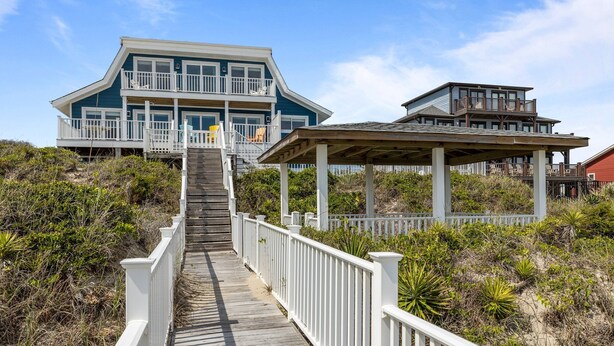 A coastal house with a wooden deck leading to a balcony, surrounded by vegetation. - Dog-friendly 5BR Beach Home with Pool & Ocean Views (Emerald Isle)