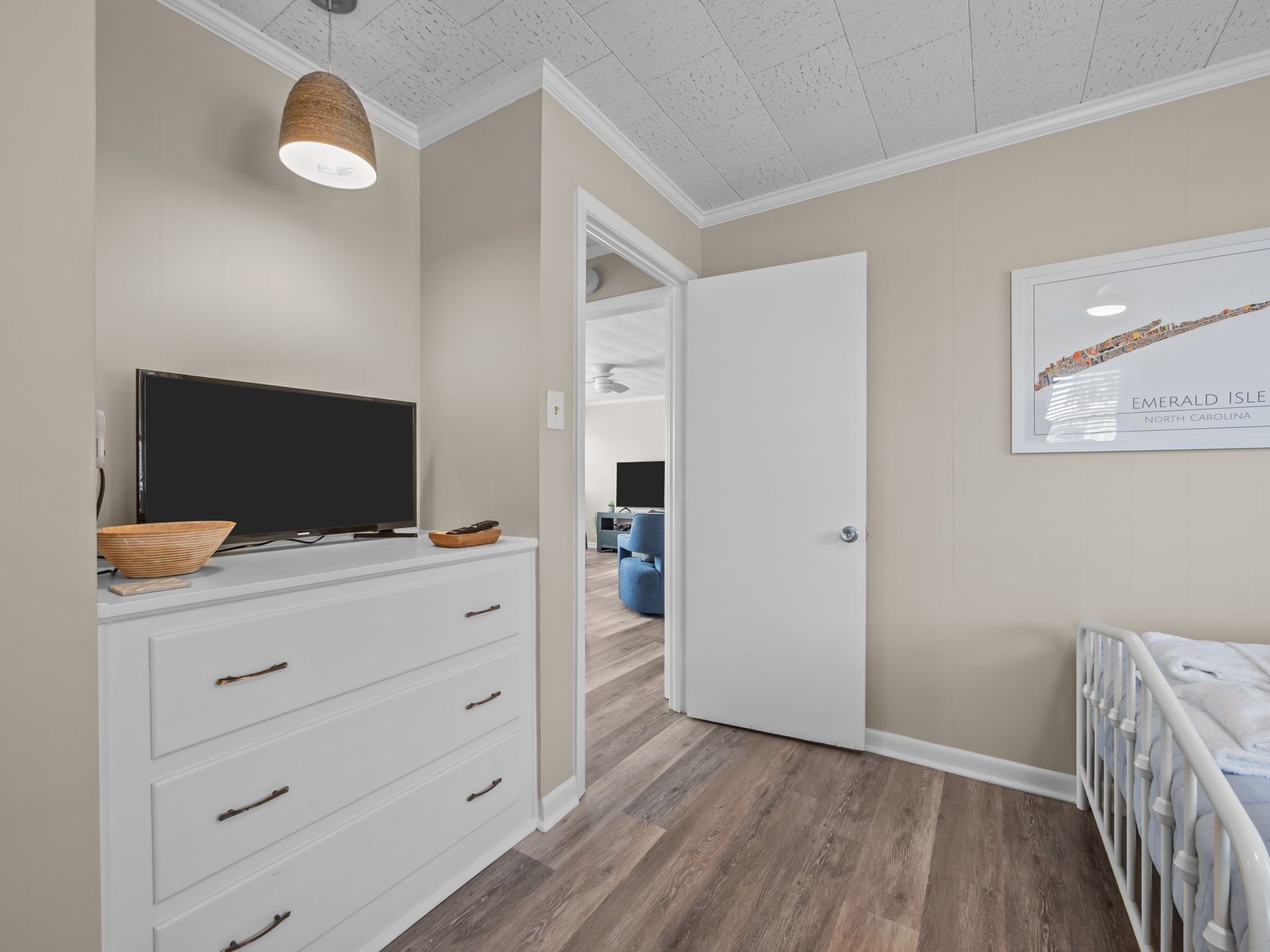 A bedroom with a television, a dresser, a door leading to another room, and a framed map on the wall.