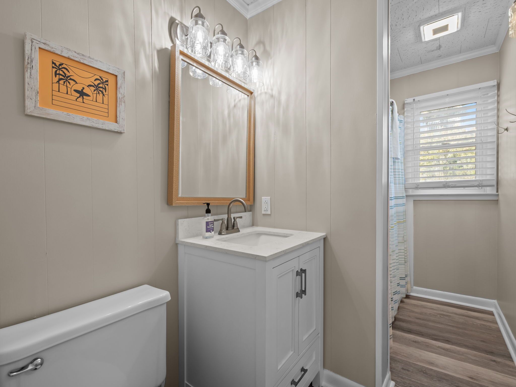 A bathroom with a white sink, a mirror, and a framed picture on the wall.