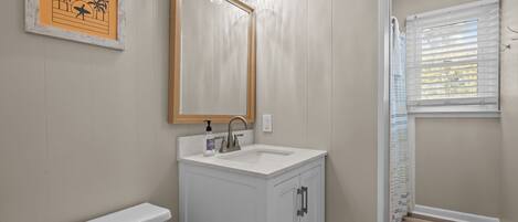 A bathroom with a white sink, a mirror, and a framed picture on the wall.