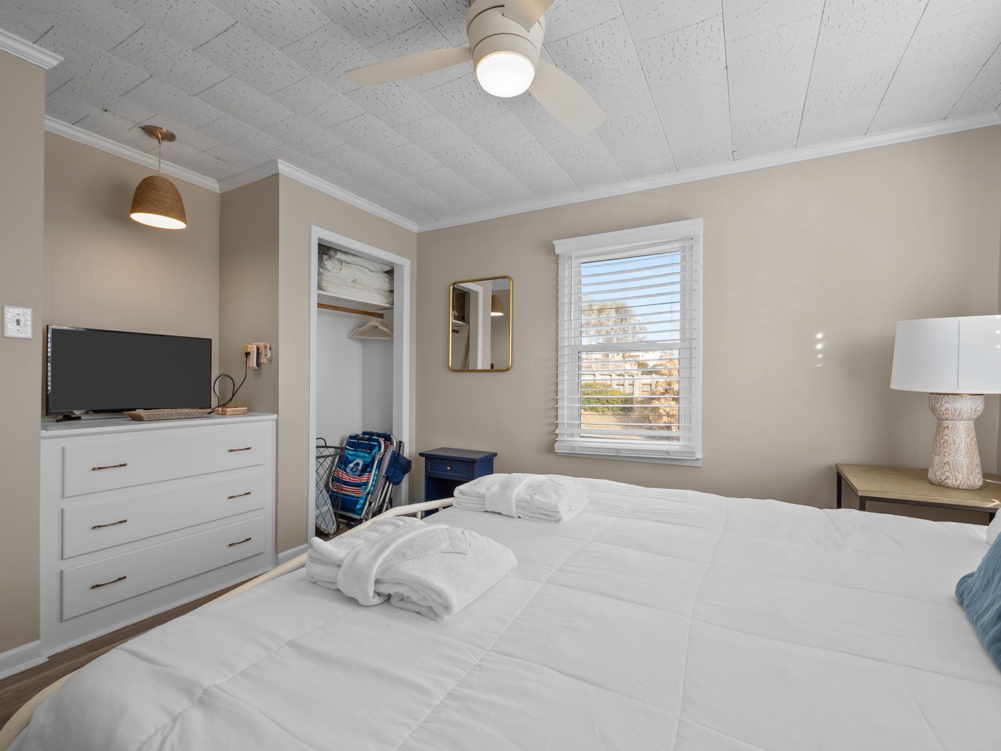A bedroom with a bed, a television, a wardrobe, a mirror, a window, and a ceiling fan.