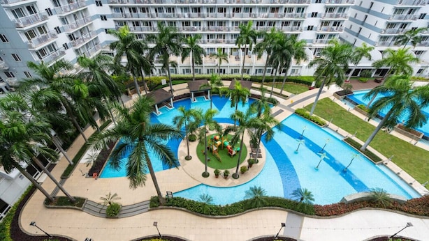 A multi-story hotel with a central swimming pool surrounded by palm trees and a children's play area. - Brand New Luxe Japandi w Pool View MOA 15 min NAIA (Pasay City)