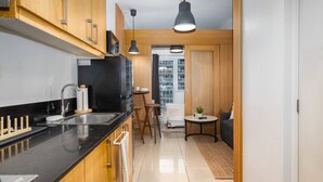 A modern kitchen with wooden cabinets, a black countertop, and a dining area with a small table and chairs. - Brand New Luxe Japandi w Pool View MOA 15 min NAIA (Pasay City)