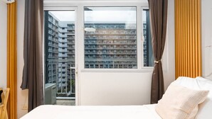 A bedroom with a bed, curtains, a window, and a view of a high-rise building. - Brand New Luxe Japandi w Pool View MOA 15 min NAIA (Pasay City)