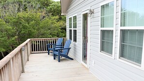 Une terrasse en bois avec deux chaises bleues et une table, une balustrade en bois, et une maison avec un revêtement blanc et de grandes fenêtres.