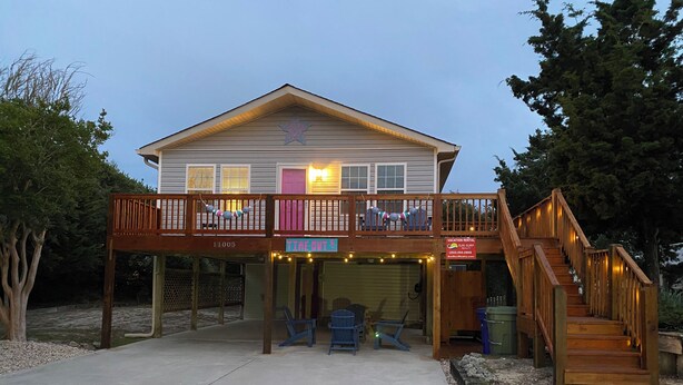 Une maison à deux étages avec un balcon, une enseigne indiquant qu’il s’agit d’une location de vacances, et un escalier menant à l’étage supérieur.