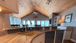Una cocina con encimera de granito, armarios blancos, lavavajillas y ventilador de techo.