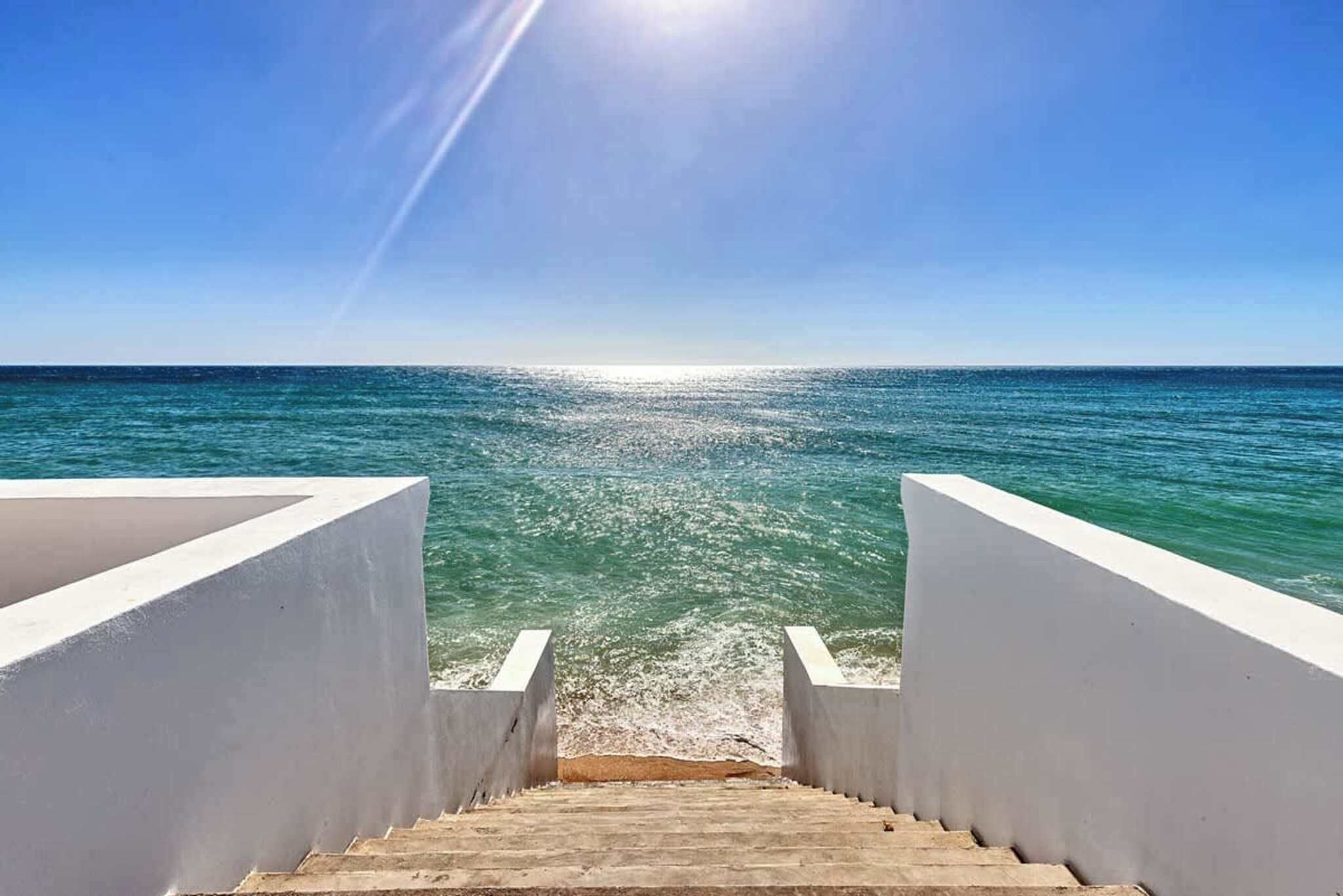 A staircase leading to a beach with a clear sky and calm sea.