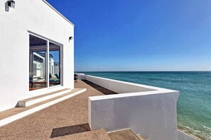 A modern white building with a glass door leading to a room, a clear view of the ocean, and a concrete structure in the foreground. - Casa del Espíritu | 8BR Beachfront | Sleeps 16 (Puerto Peñasco)