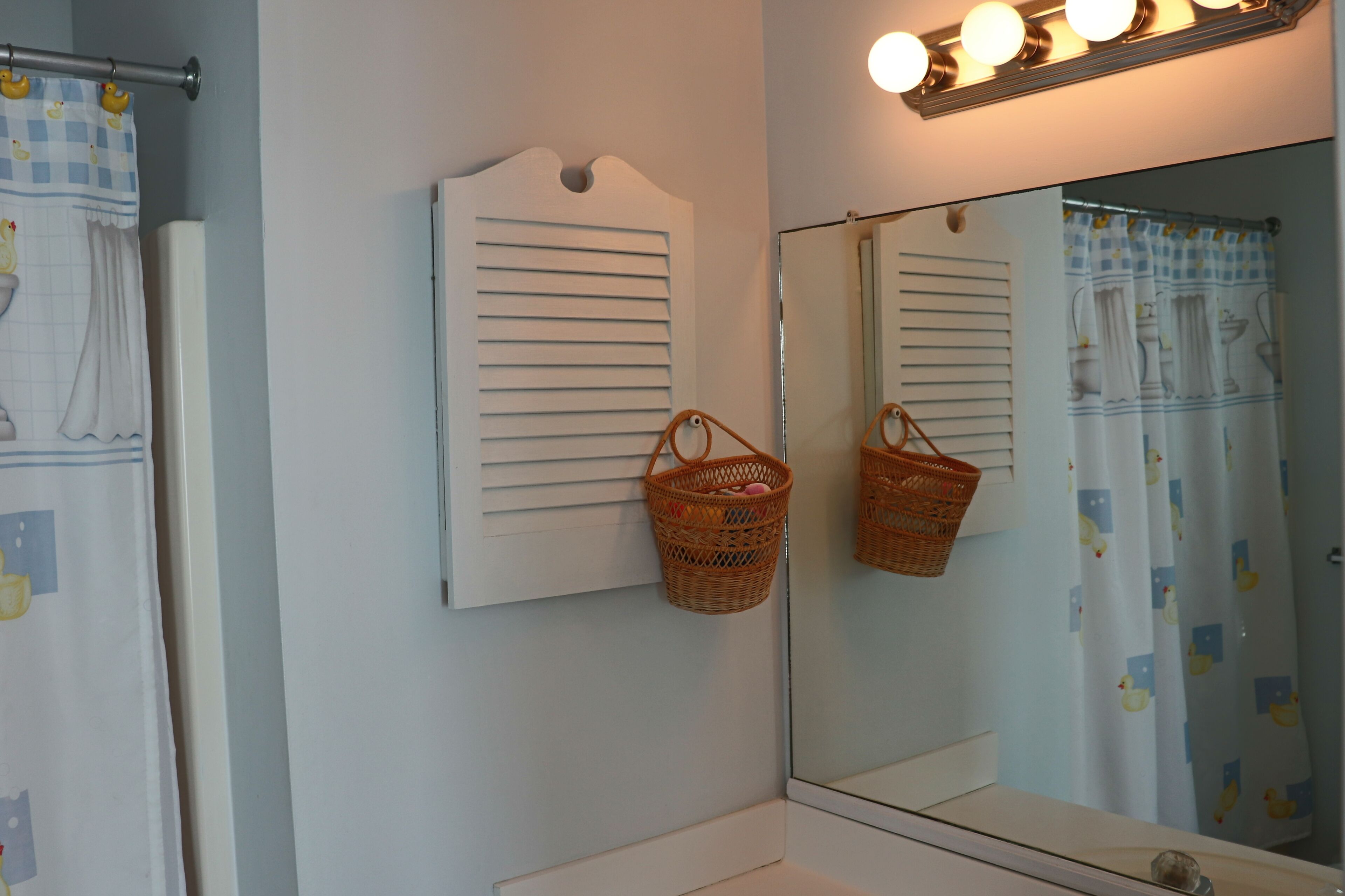 A bathroom with a mirror, two wicker baskets, and a light fixture above the mirror.