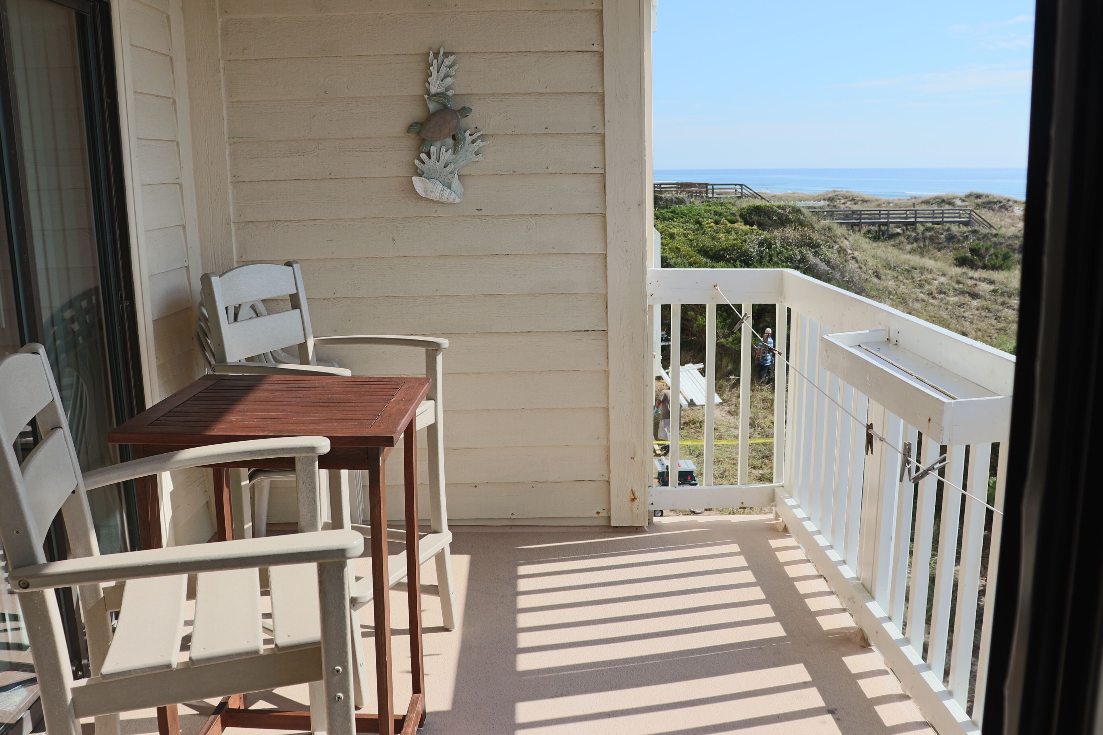 Ein Balkon mit Tisch und Stühlen, einem Ziergegenstand an der Wand und Blick auf Strand und Dünen.