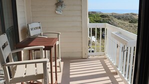 Ein Balkon mit Tisch und Stühlen, einem Ziergegenstand an der Wand und Blick auf Strand und Dünen.
