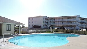 Ein Schwimmbecken mit Betonrondell, Holzlattenzaun und einem mehrstöckigen Gebäude im Hintergrund.