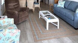 Ein Wohnzimmer mit einer Couch, Sesseln, einem Couchtisch und einer Küchenzeile mit Schränken und Geräten.