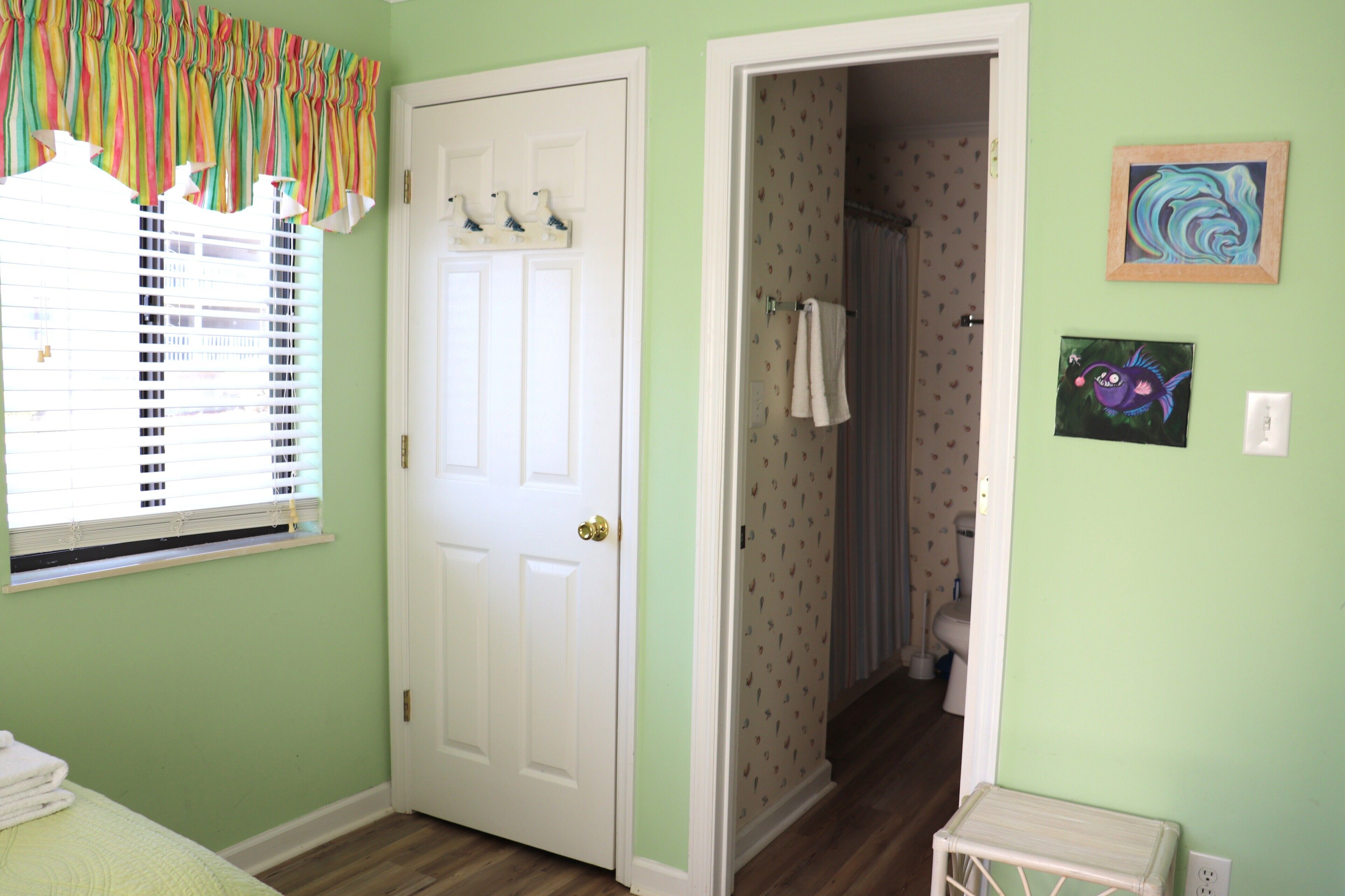 A room with a door, a window with blinds, a small table, and a wall with two framed pictures.