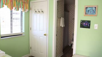 A room with a door, a window with blinds, a small table, and a wall with two framed pictures.