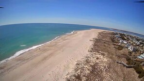Luchtbeeld van een strand met heldere lucht, een zandstrand en een woongebied met huizen en een pier.