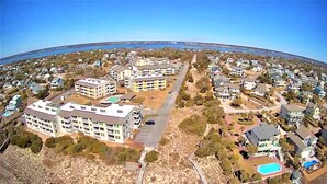Vista aèria d'una zona residencial amb diversos edificis d'apartaments, una carretera central i una massa d'aigua al fons.