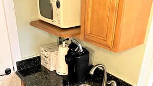 Cuina compacta amb microones integrat, una rentavaixelles i una cafetera a la superfície.