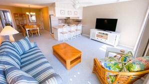 Una sala de estar con sofá, mesa de centro, mueble para televisión y un comedor con sillas y mesa.