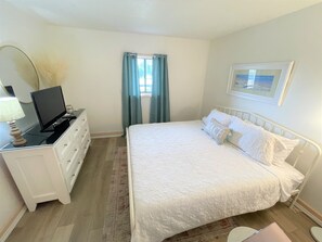 A bedroom with a bed, a dresser, a television on the dresser, and a window with curtains.