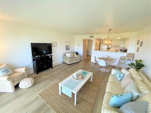 A living room with a TV, sofa, coffee table, and a dining area with chairs and a table.