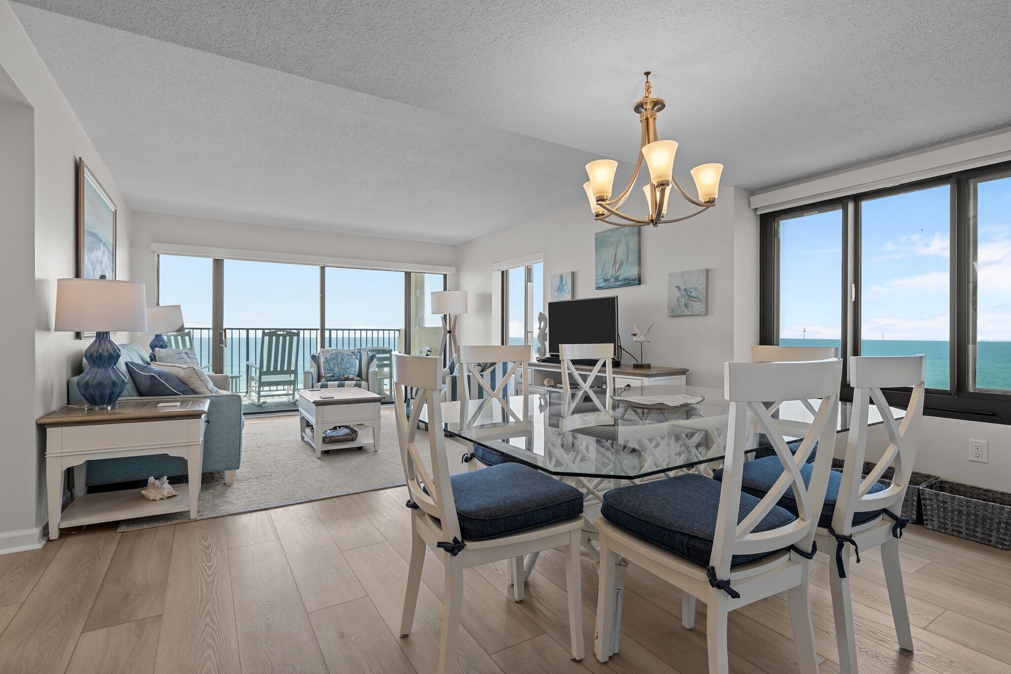 A spacious room with a large dining table, white chairs, a chandelier, and a view of the ocean.