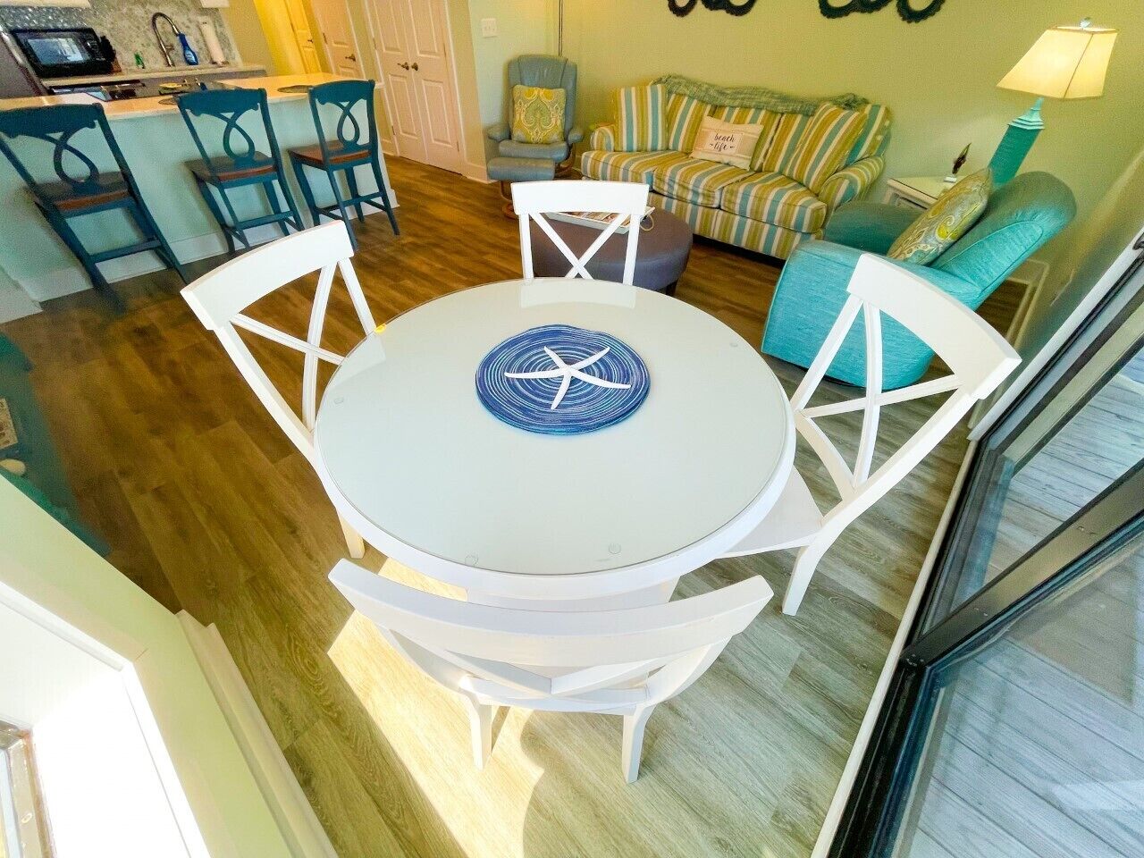 A dining area with a round table and four chairs, a kitchen area with a microwave and sink, and a living room with striped sofas and a couch.