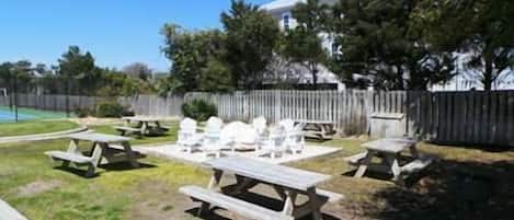 Picnicområde med borde og stole, omgivet af et træhegn og træer.