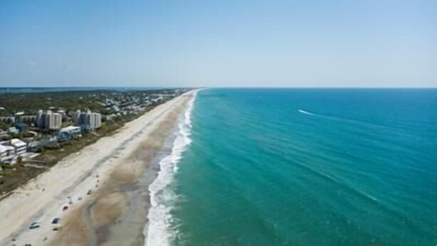 A coastal view with a beach, ocean, and buildings along the shore. - Your Slice of Oceanfront Paradise at Queens Court (Emerald Isle)