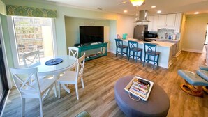 A modern living room with a dining area, a kitchen, and a balcony. - Your Slice of Oceanfront Paradise at Queens Court (Emerald Isle)