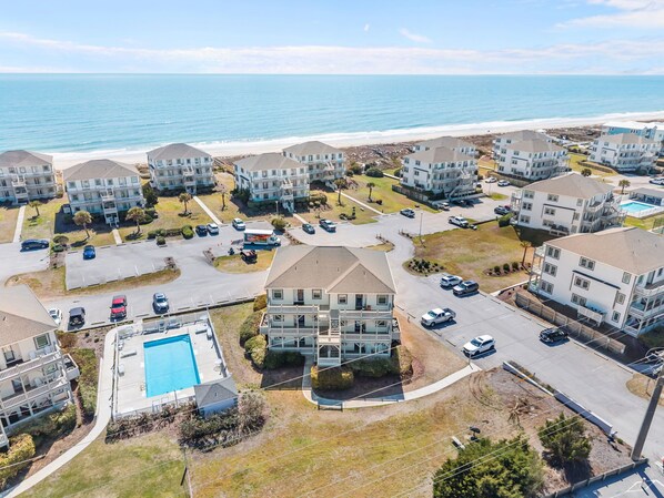 Un quartier résidentiel situé sur la côte, composé de plusieurs maisons à deux étages, d’un bâtiment central doté d’une piscine et, au loin, d’une plage.