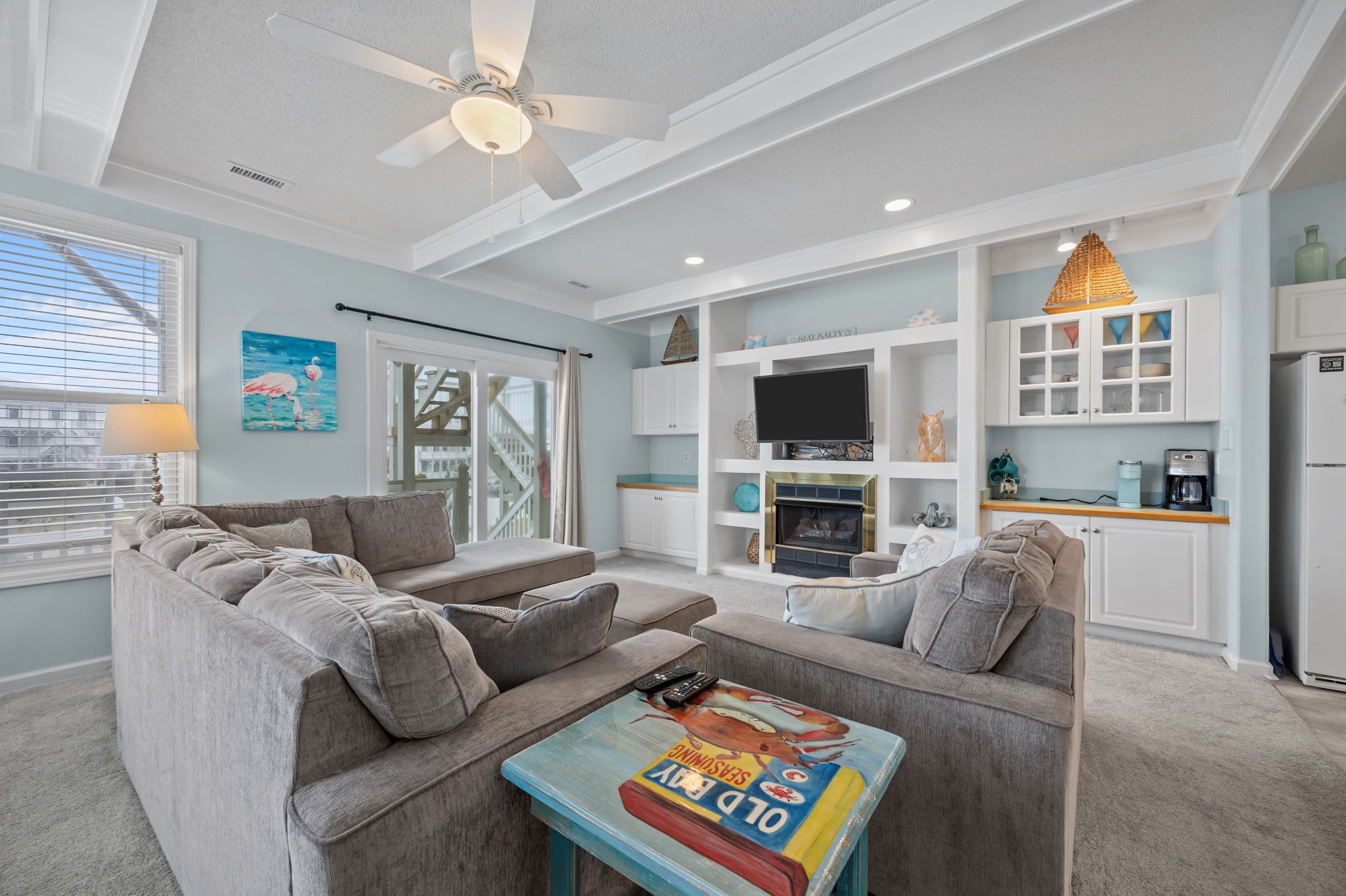 A living room with a gray sofa, a coffee table with a magazine, a ceiling fan, and a TV.