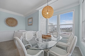 Una zona de menjador amb taula de vidre, cadires de vimetla, una cistella de vimetla i una làmpada penjant de fibra.