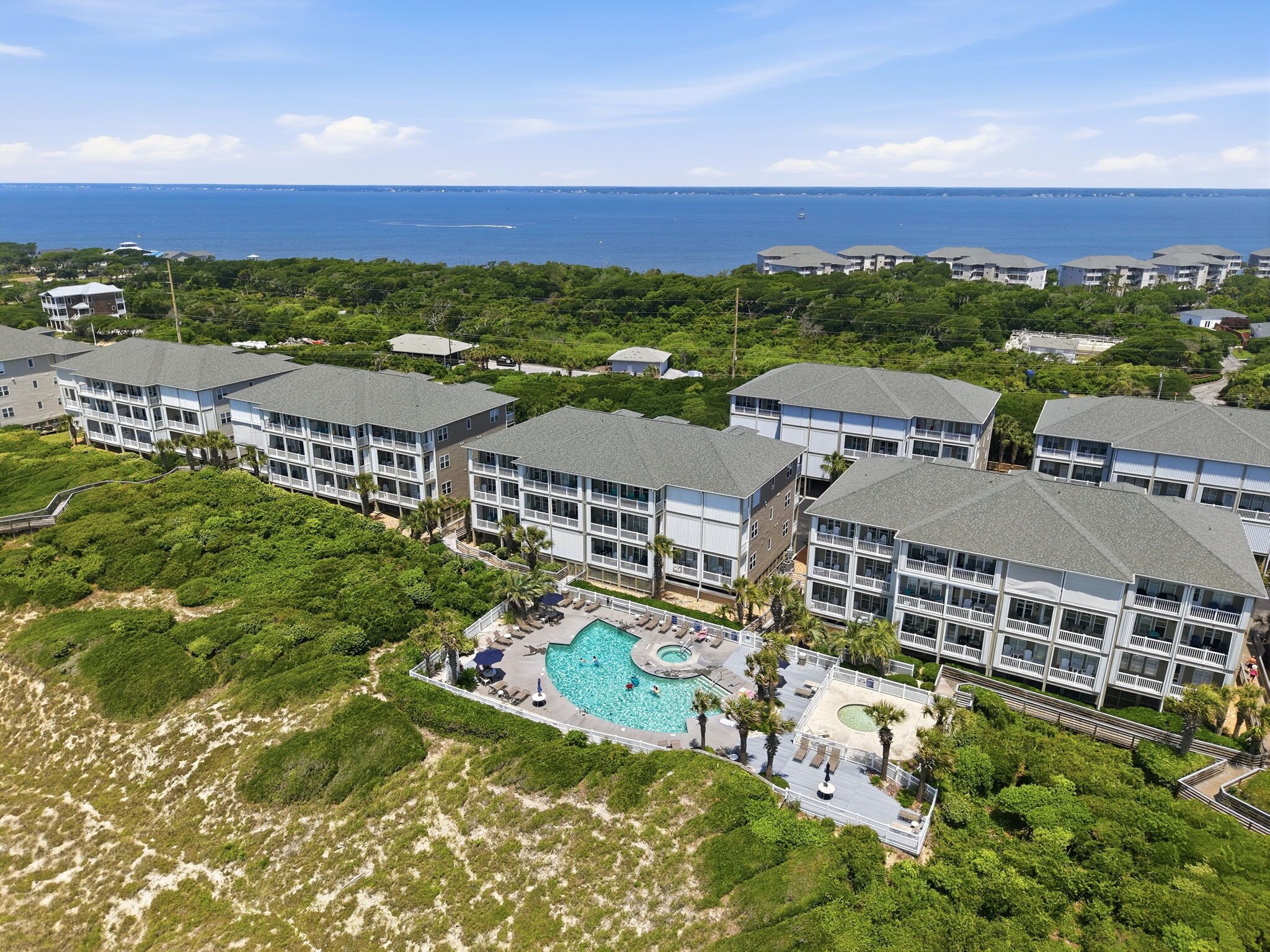 A resort with multiple buildings, a central pool area, and a view of the ocean.