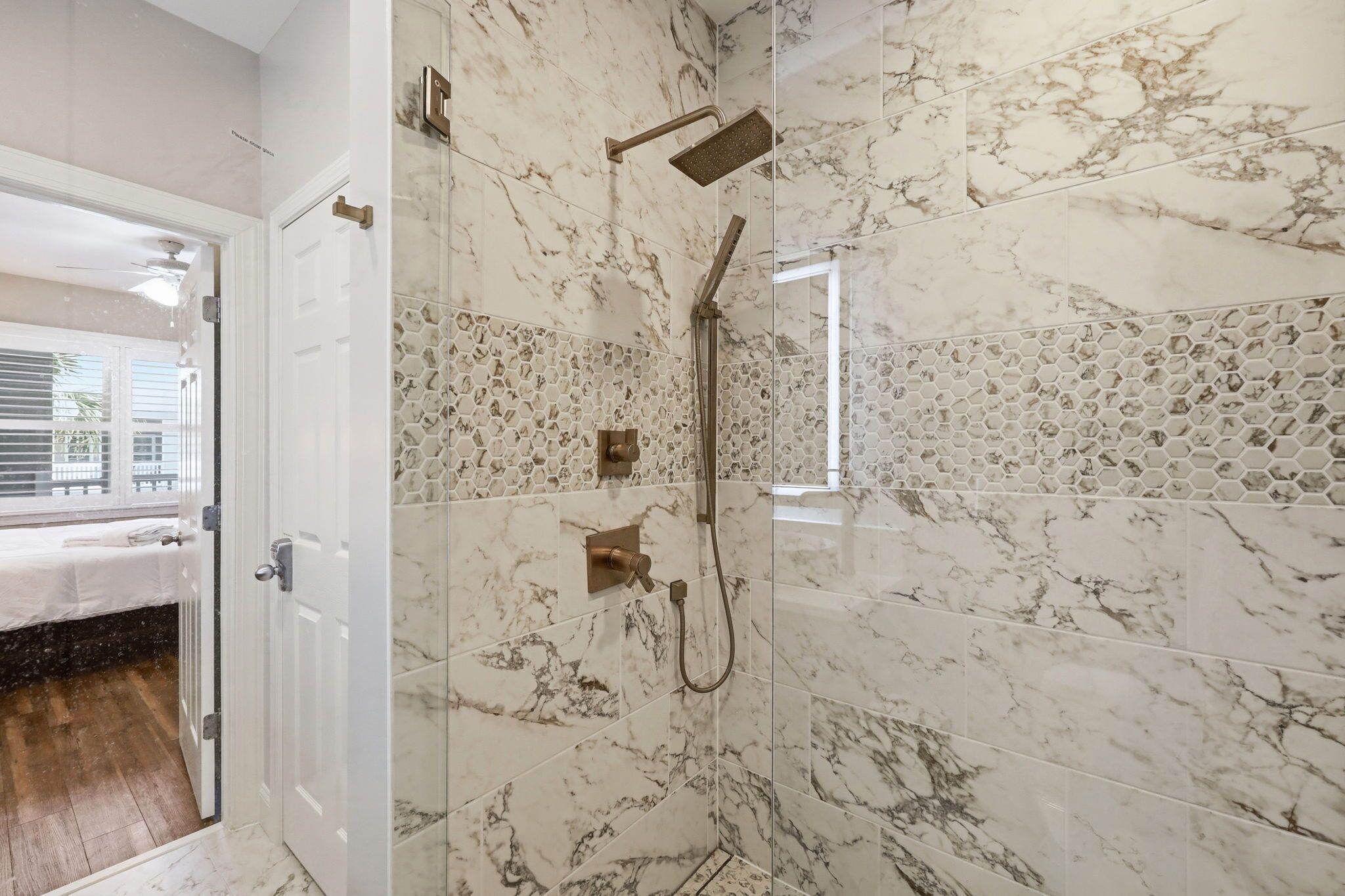 A bathroom with marble tiles, a shower with a handheld showerhead, and a hexagonal mosaic tile pattern on the wall.