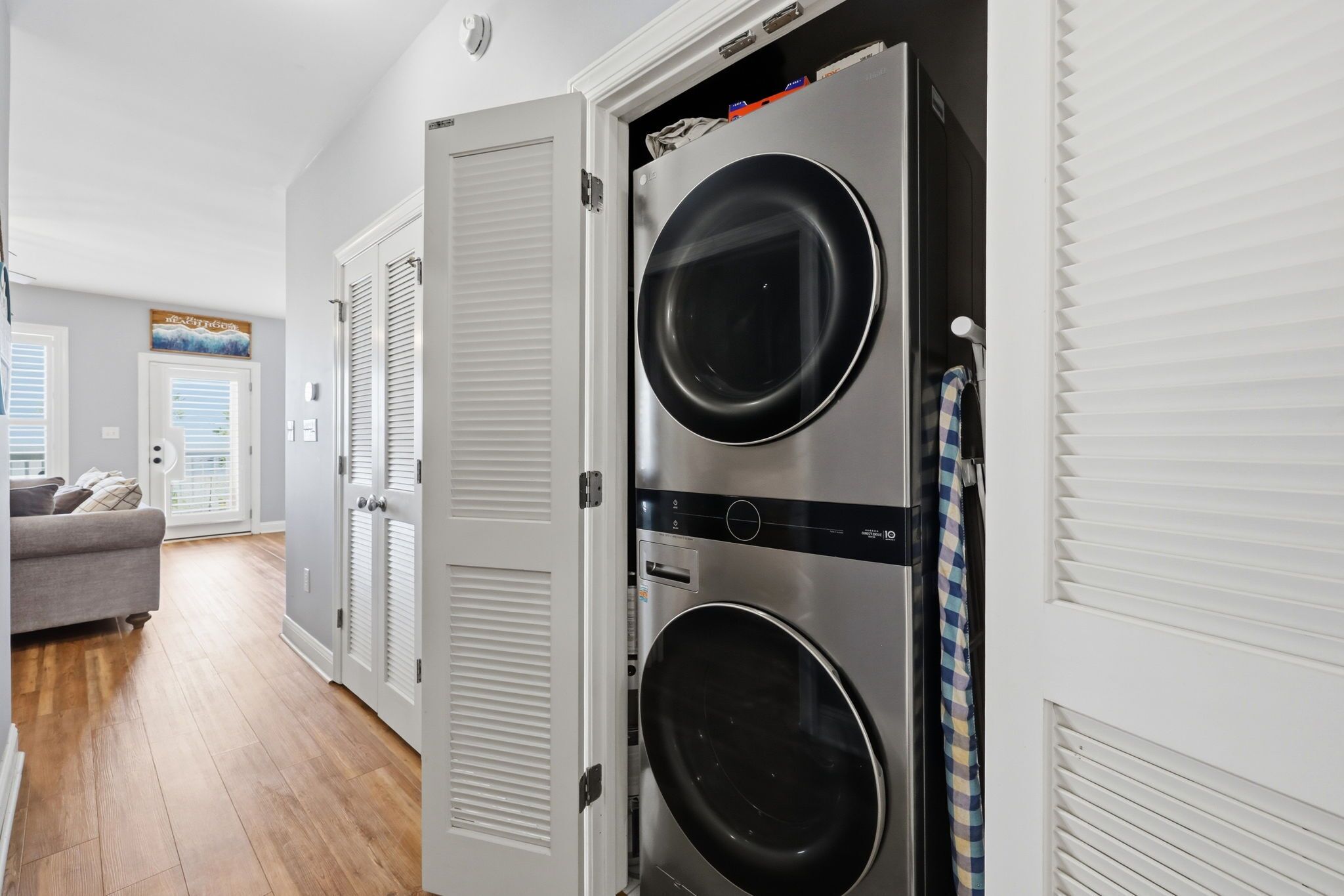A laundry room with two stacked washers and dryers, a gray couch, and a door leading to another room.