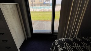 A room with a view of a swimming pool, a balcony, and a building in the background.