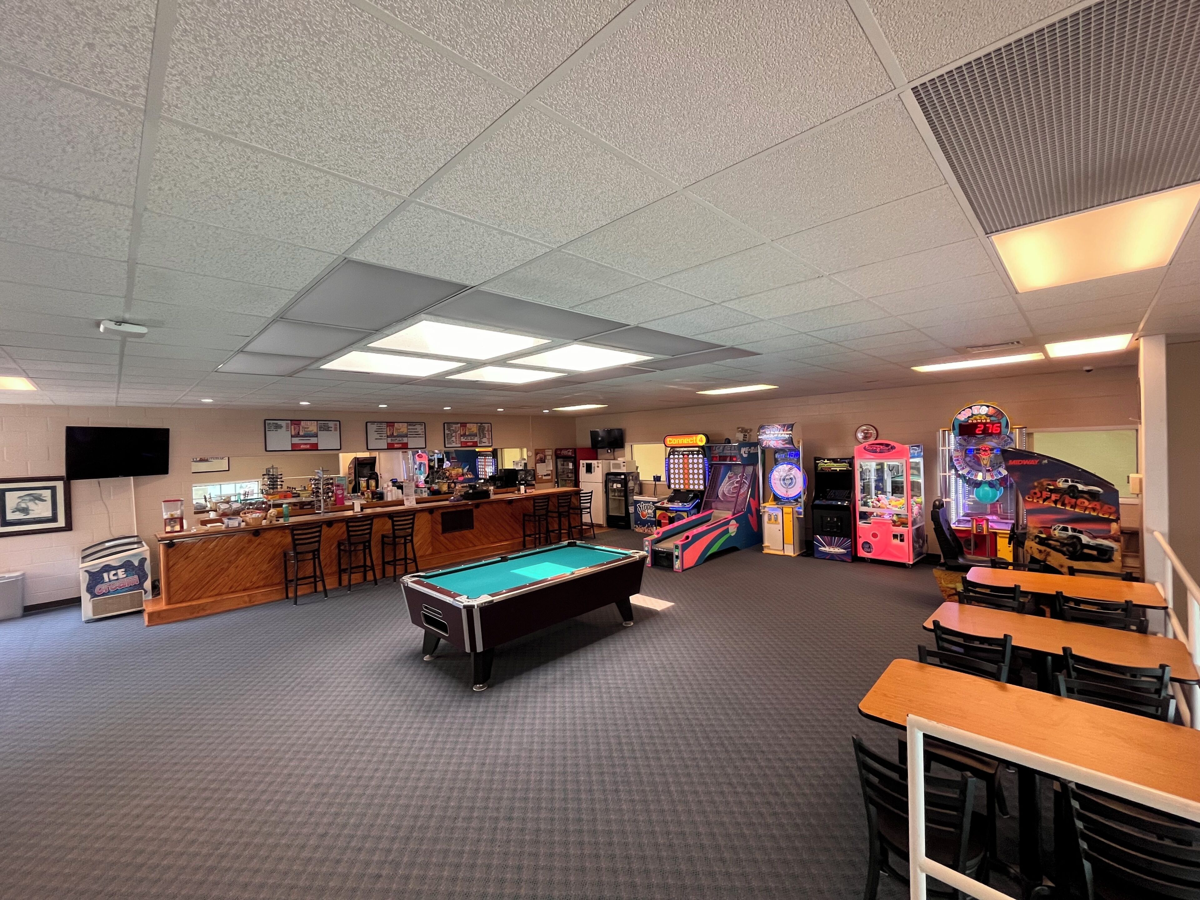 A pool table in a room with a bar area, arcade games, and multiple tables and chairs.